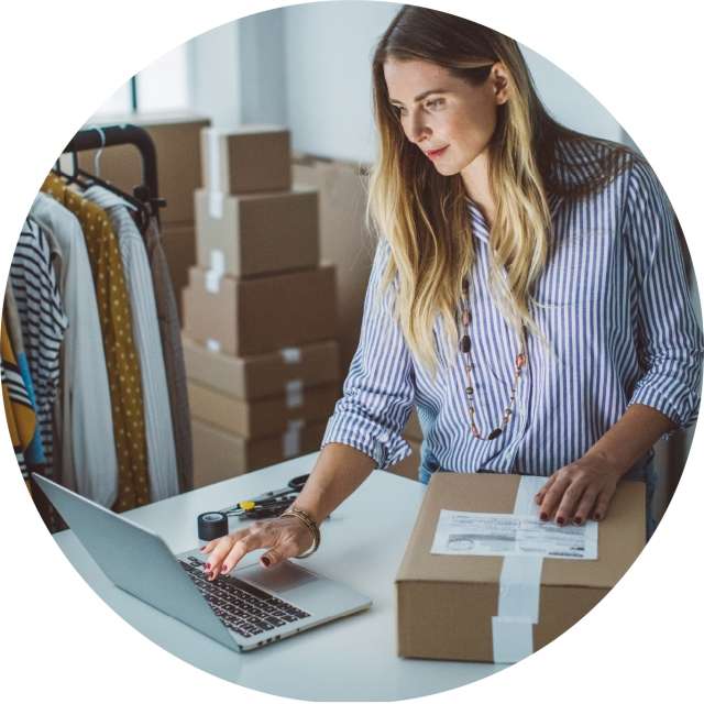 Woman typing on laptop while sealing box for shipping